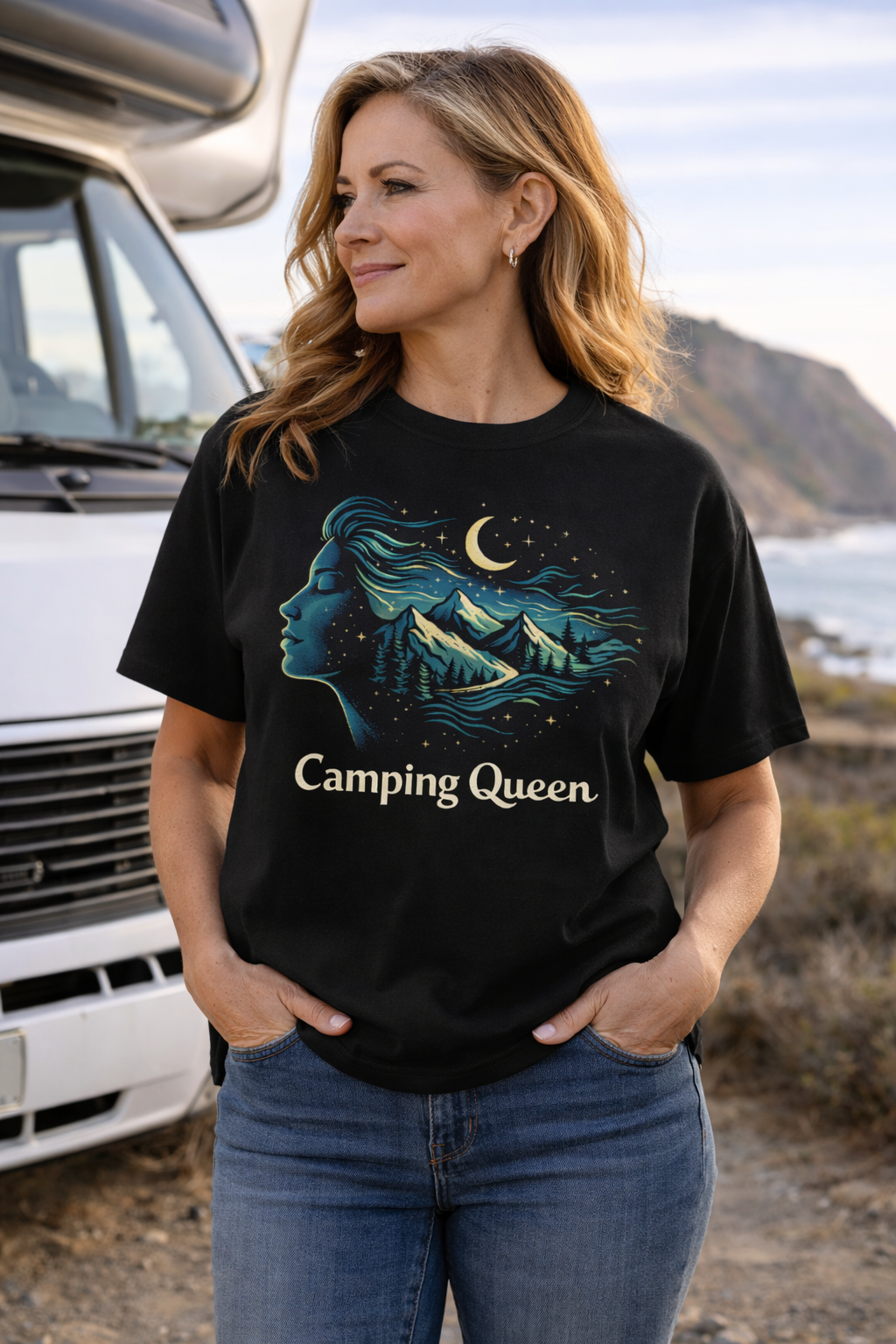 Camping Queen-Mond-Sterne-Berge. Frau Mitte 50 trägt schwarzes Camping-Queen T-Shirt mit Berg- und Nachtmotiv, steht vor Wohnmobil an der Küste – stilvolle Campingmode für selbstbewusste Camperinnen.